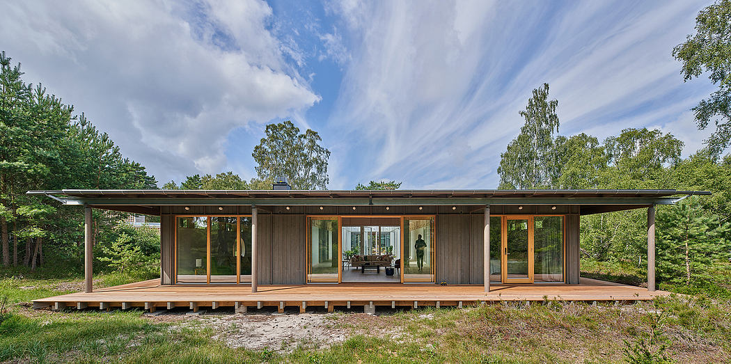 A modern, wood-paneled vacation home with floor-to-ceiling windows, nestled in a forested setting.