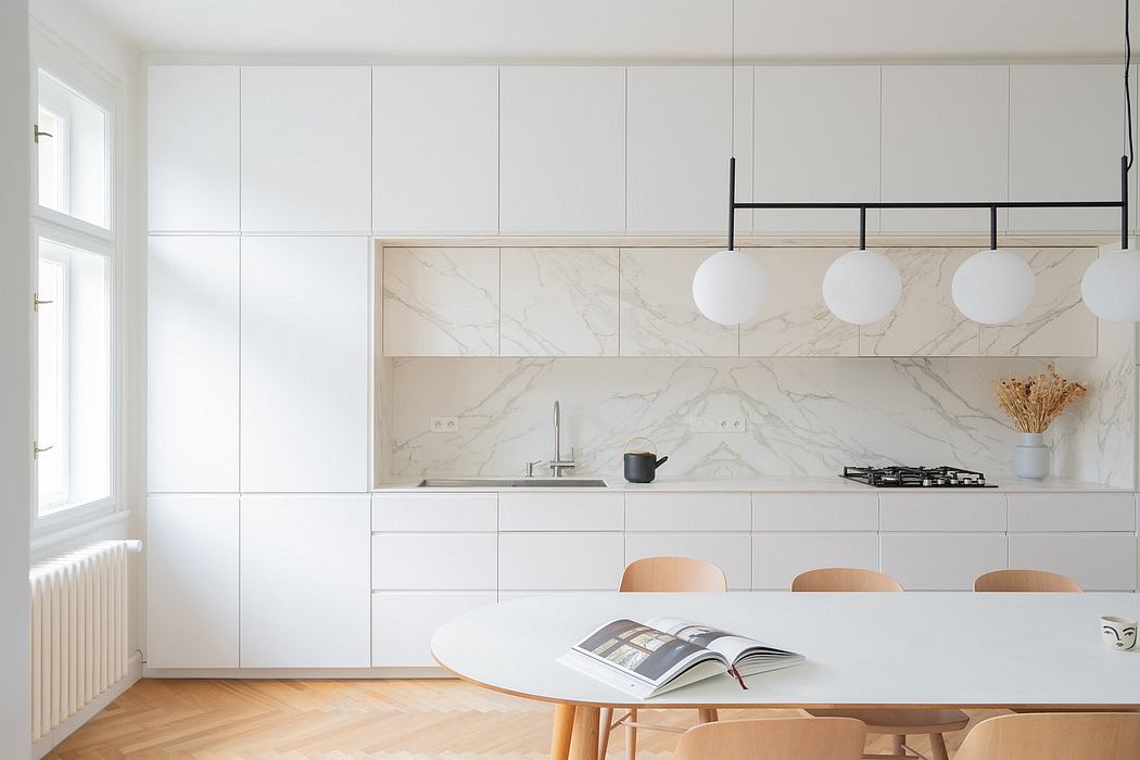 Bright, minimalist kitchen with marble backsplash, sleek white cabinetry, and pendant lighting.