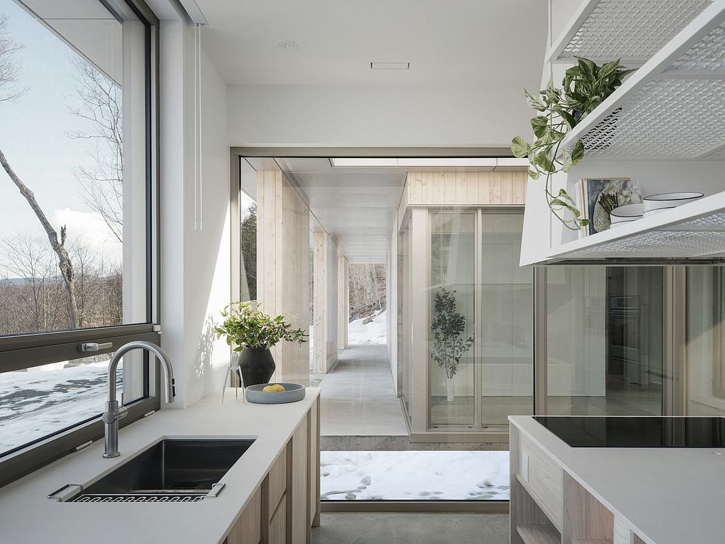 A modern kitchen with sleek wood cabinets, marble countertops, and floor-to-ceiling windows offering scenic views.