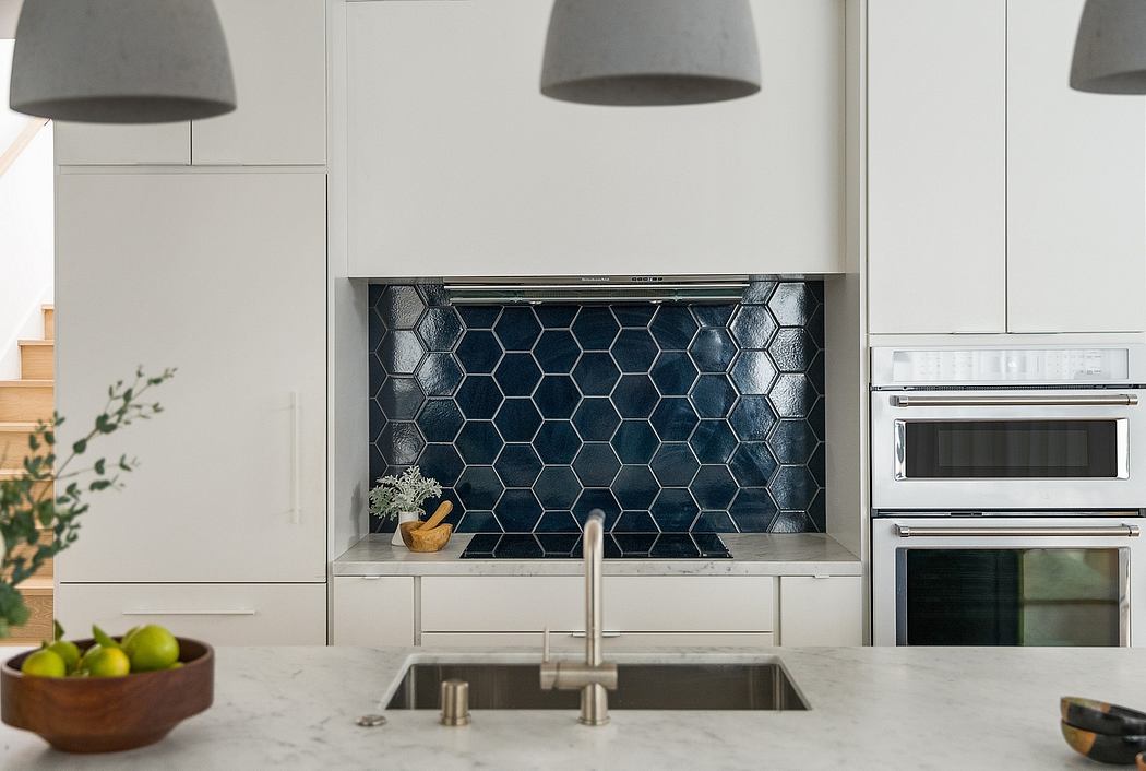 Modern kitchen with sleek white cabinets, hexagon-patterned blue backsplash, and pendant lighting.