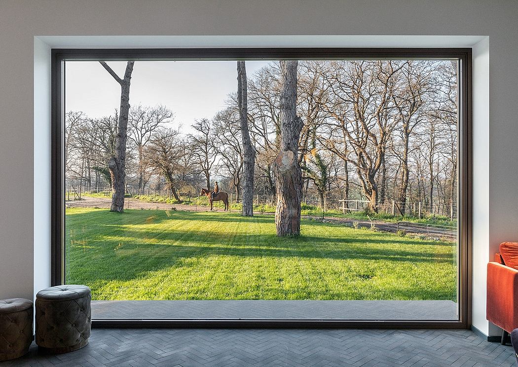 Large window frames a picturesque rural landscape with a grassy meadow, trees, and horses.