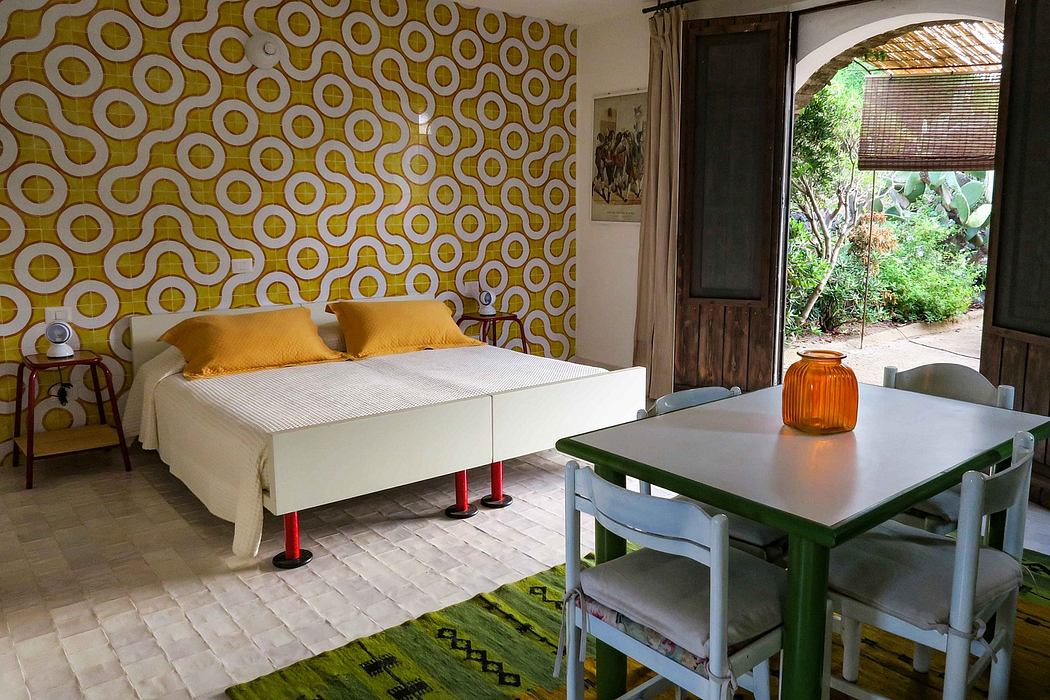 Vibrant retro-style bedroom with patterned wall, white bed, and colorful furnishings.