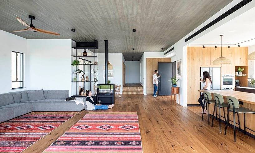 A modern, open-plan living space with exposed concrete ceiling, wooden floors, and colorful area rug.