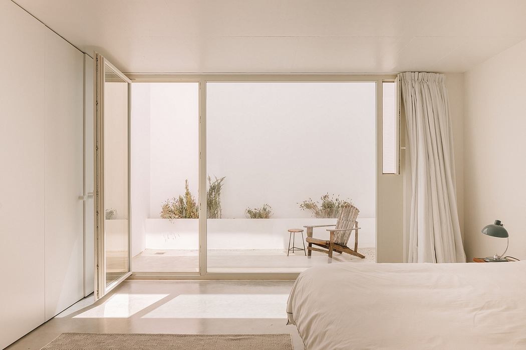 Serene minimalist bedroom with large windows, wooden accents, and a view of the outdoors.