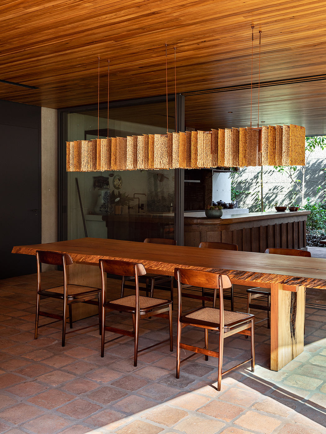 Rustic wooden dining area with a bold chandelier, featuring a stone tile floor and a tiered bar counter.