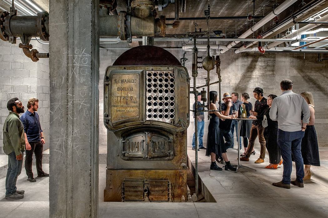 An industrial space with vintage boiler and a group of people gathered around, discussing.