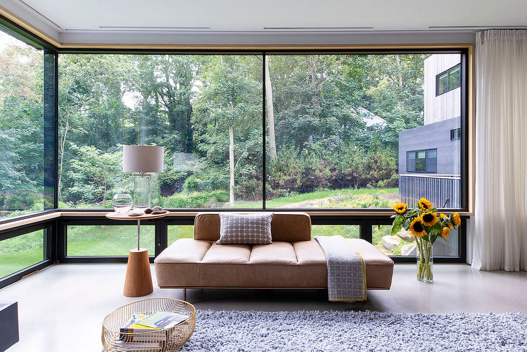 Modern living room with expansive glass walls, neutral furnishings, and lush greenery outside.