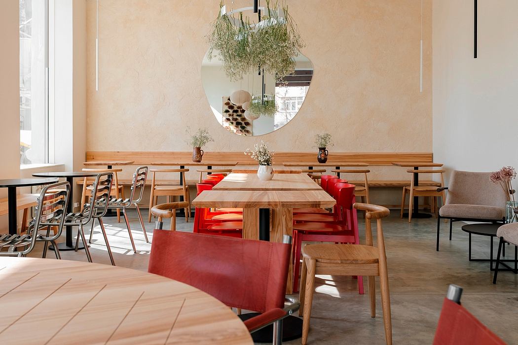 Minimalist cafe interior with wooden tables, red chairs, and a large round mirror above.