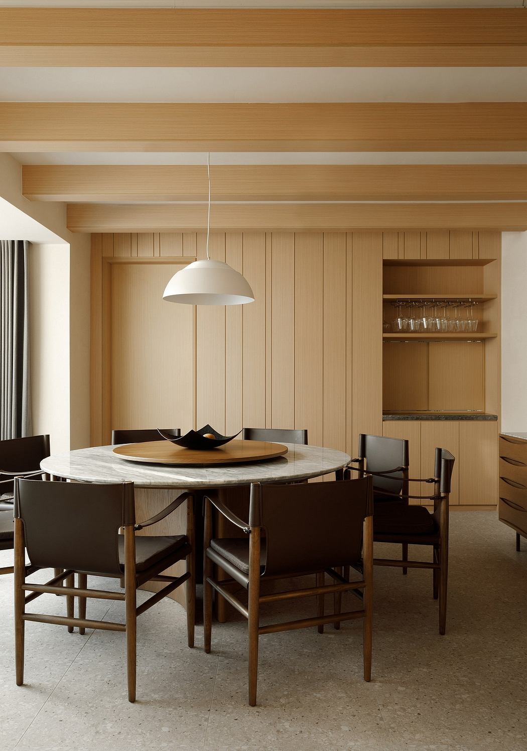 Warm wood paneled ceiling and walls, round marble dining table, matching dark chairs.