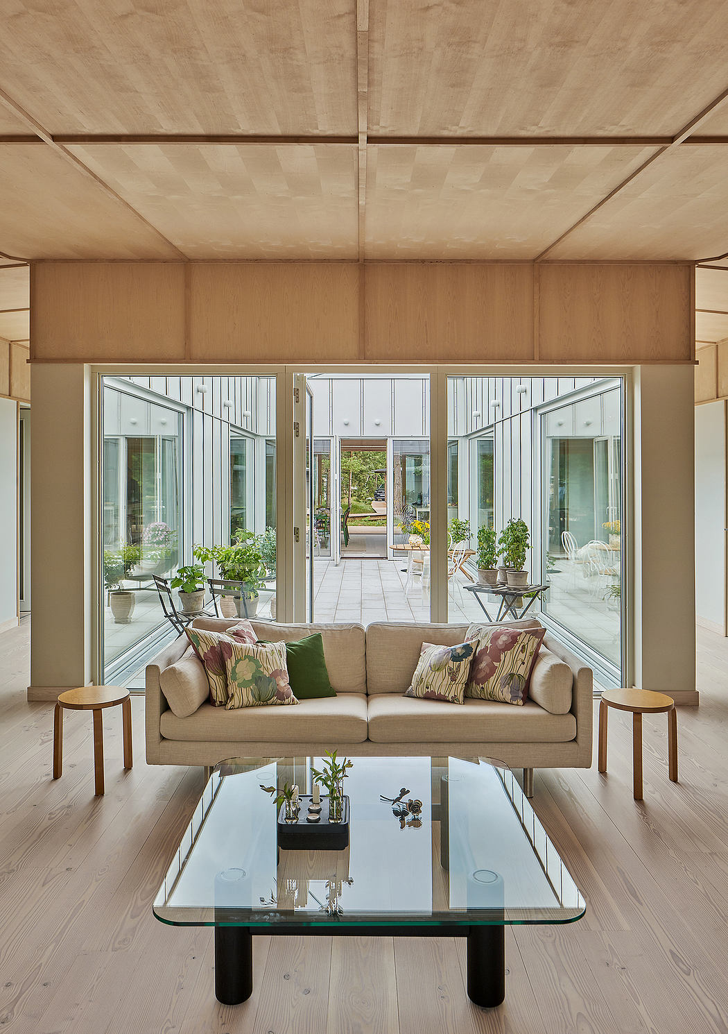 Spacious living room with large glass doors, wood paneled walls and ceiling, and glass coffee table.