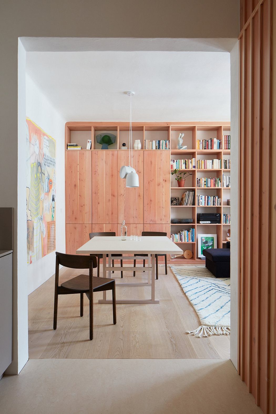 A modern, minimalist living space with natural wood cabinetry and a built-in bookshelf.