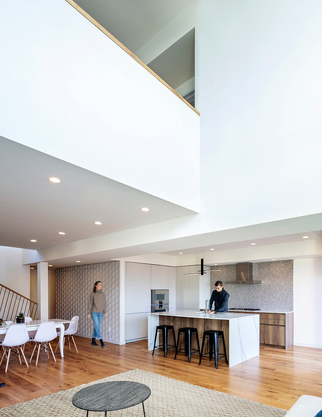 A modern, open-concept kitchen and dining area with wooden floors, minimalist furnishings, and geometric patterns.