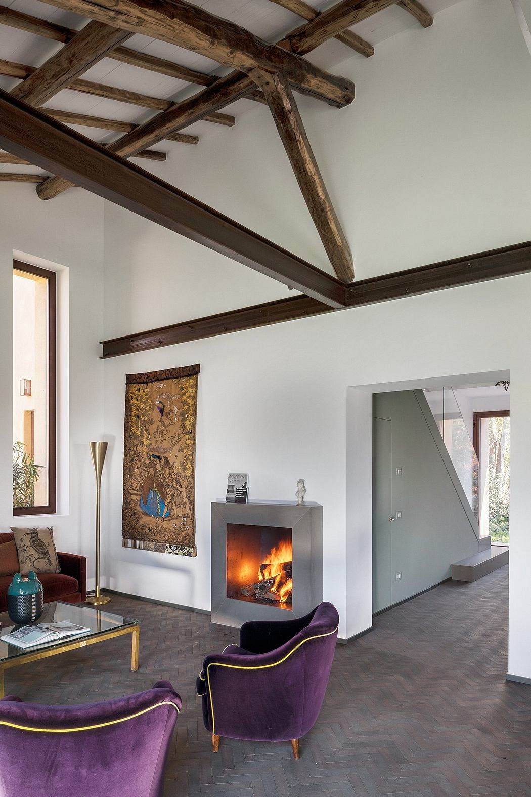 A cozy living room with exposed wooden beams, a fireplace, and plush purple chairs.