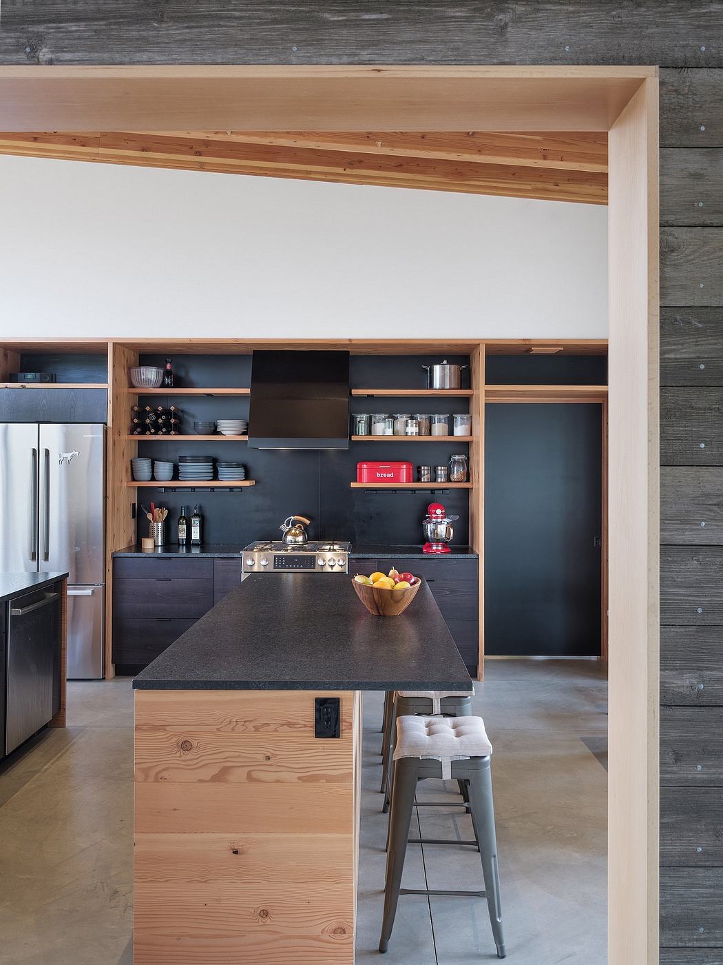 Modern, minimalist kitchen with wood and black accents, shelves, and an island.