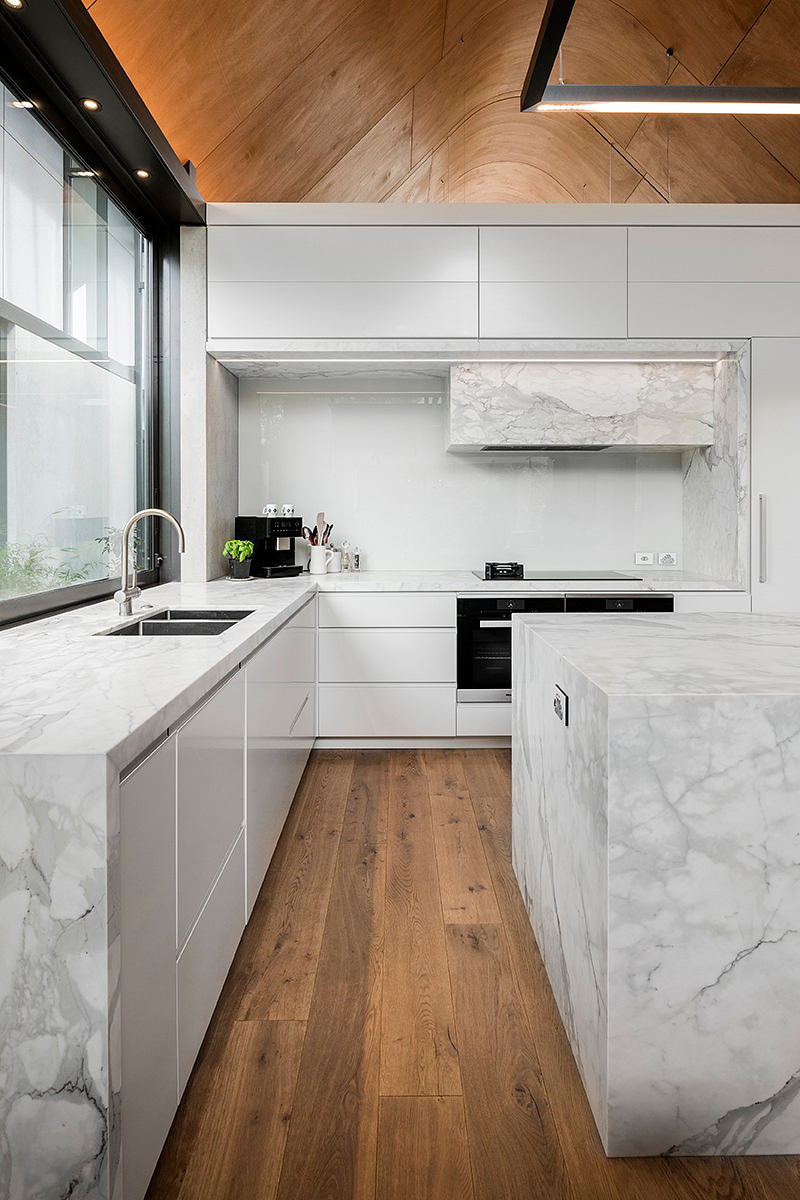 Sleek white kitchen with marble countertops, wood floors, and modern appliances.