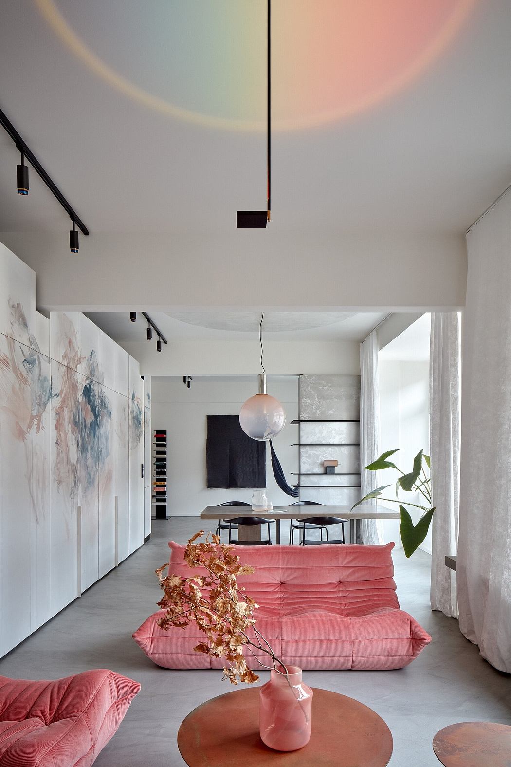 Minimalist open-concept living space with pink velvet sofa, abstract art, and modern lighting.