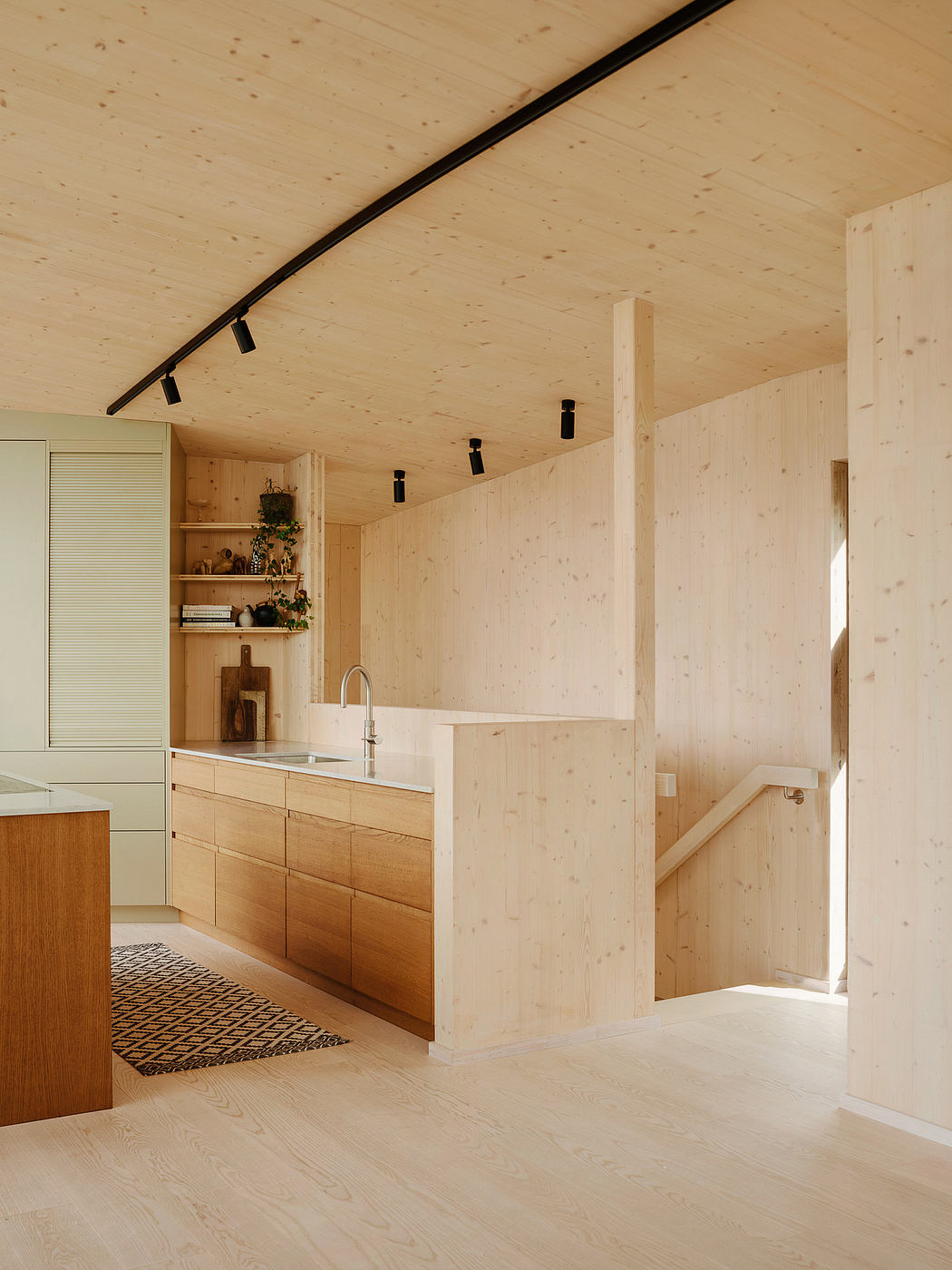 Warm, minimalist kitchen with wood-paneled walls, track lighting, and built-in shelving.