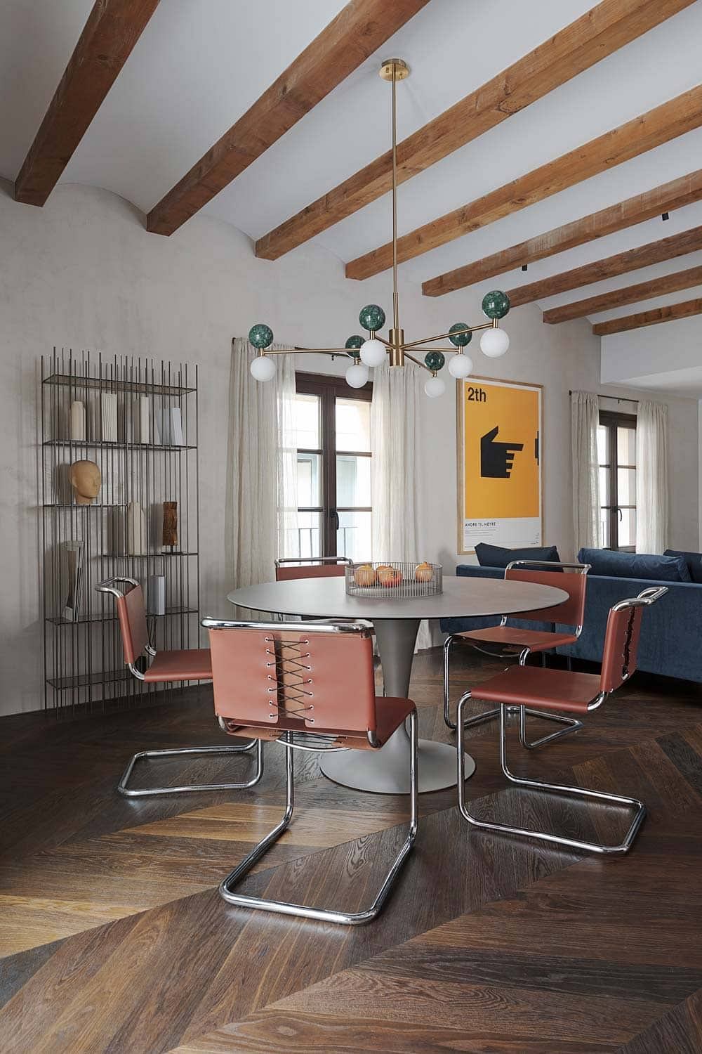 A modern dining room with wooden beams, a brass chandelier, and orange leather chairs.