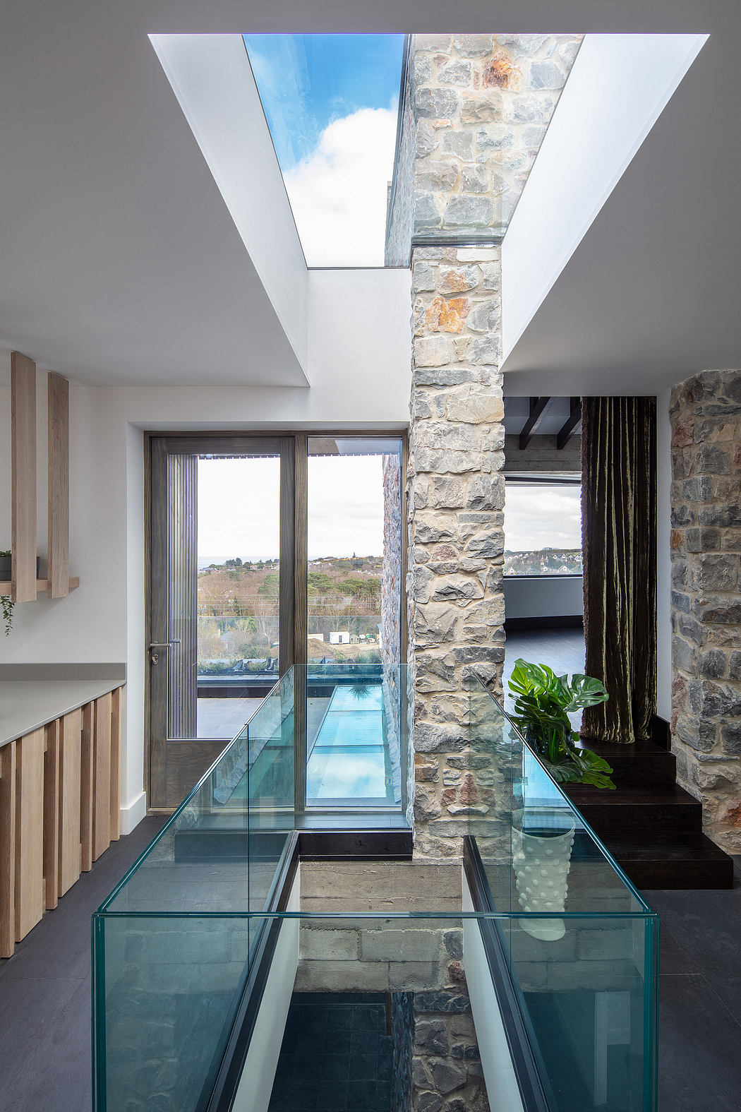 Expansive glass walls, stone column, and sleek glass floor panels create a modern, airy space.