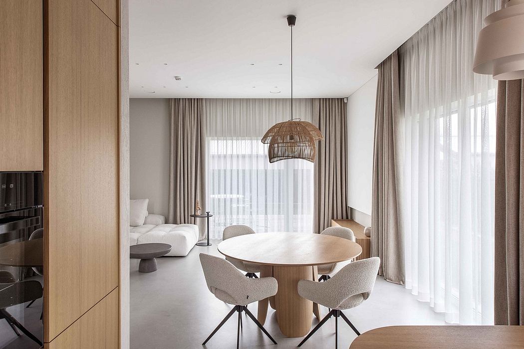 Modern, minimalist dining area with round wooden table, plush chairs, and rattan pendant light.