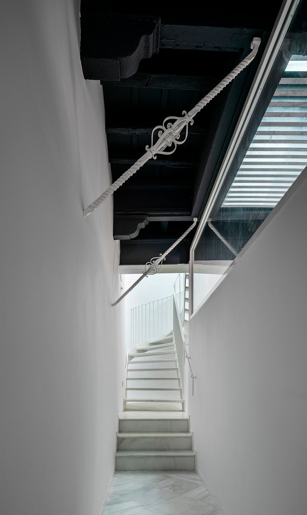 A monochromatic staircase with intricate wrought-iron railings, leading to a glass-walled balcony.