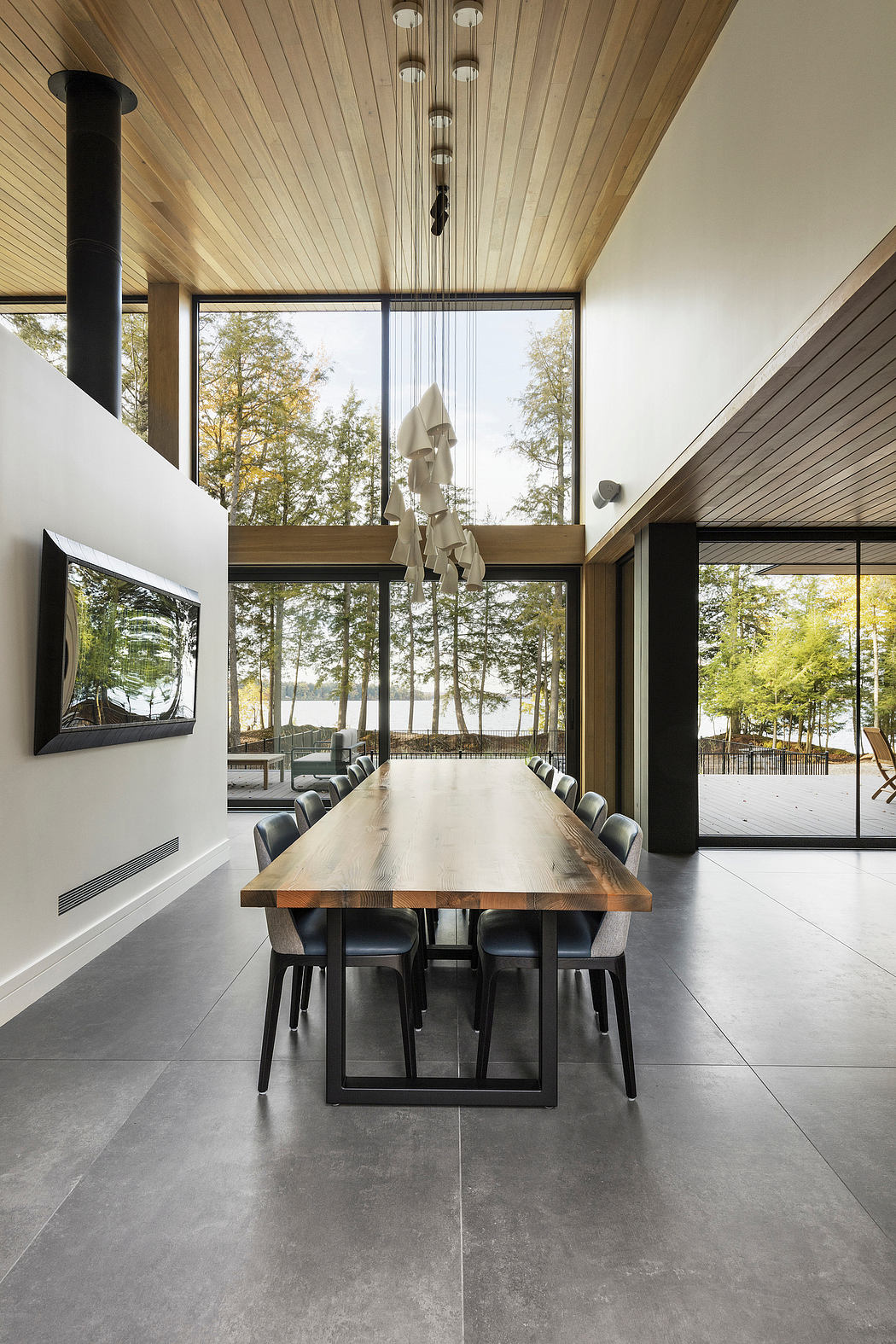 Expansive glass walls frame a modern dining area with a rustic wood table and pendant lighting.
