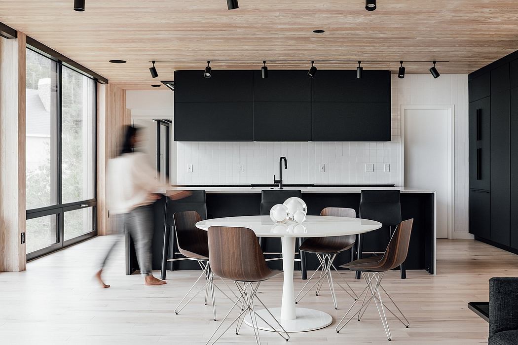 A modern kitchen with sleek black cabinetry, white countertop, and a round dining table surrounded by chairs.