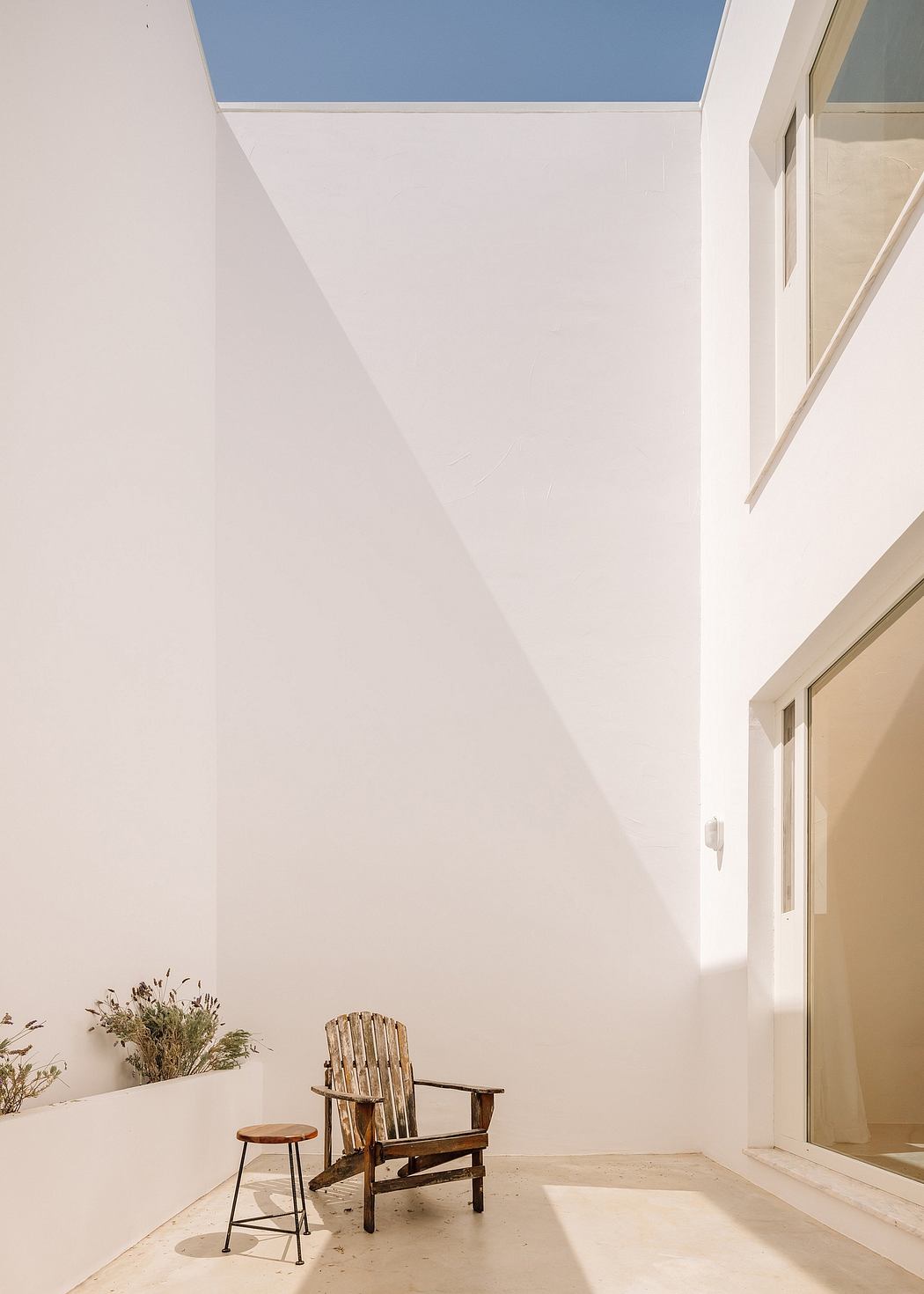 Minimalist architecture with stark white walls, wooden Adirondack chair, and small side table.