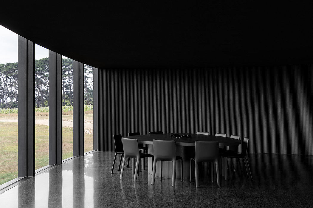 Modern architectural interior with dark, sleek furnishings and expansive windows overlooking lush greenery.