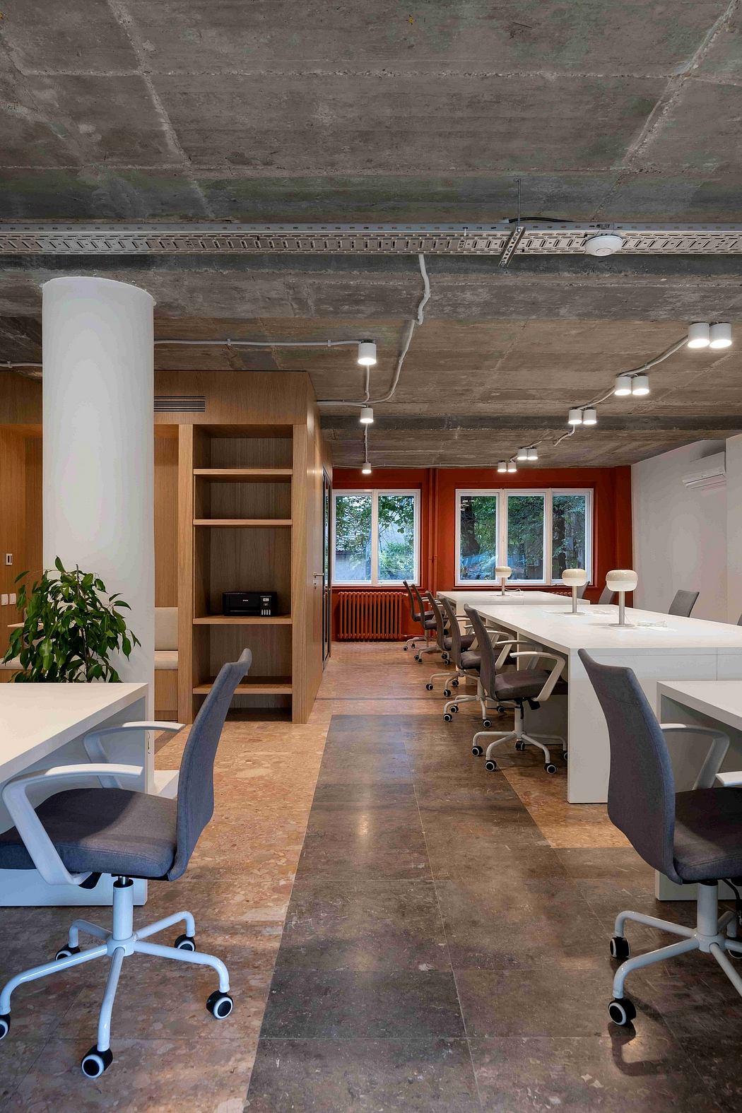 Modern open-plan office with exposed concrete walls, warm wood accents, and ergonomic chairs.
