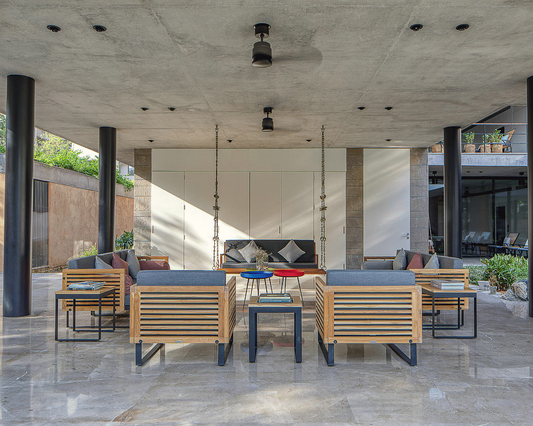 Modern outdoor lounge with concrete ceiling, wood and metal furnishings, and lush greenery.