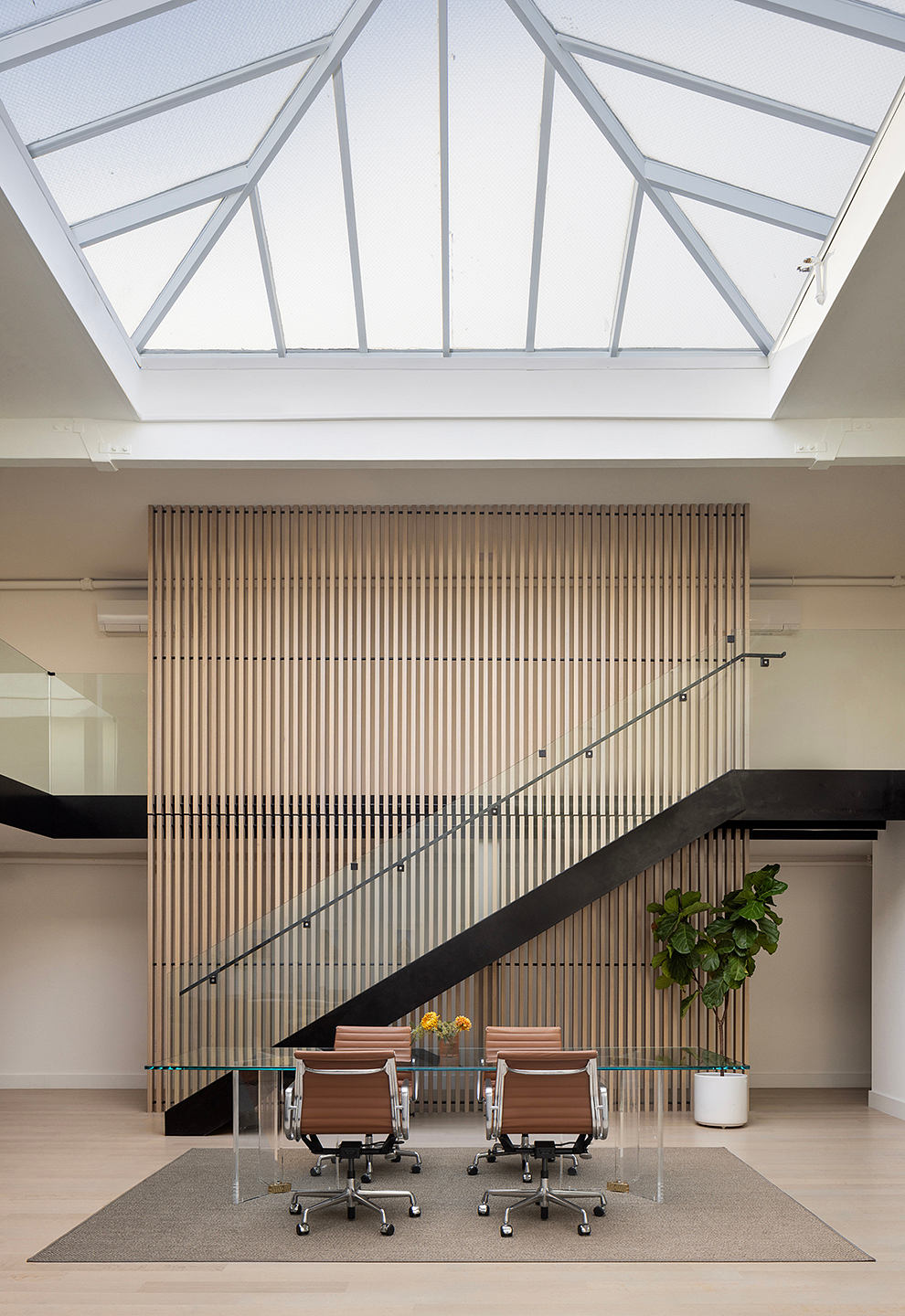 Airy glass atrium with triangular frame, contrasting wooden slat wall, and glass conference table.