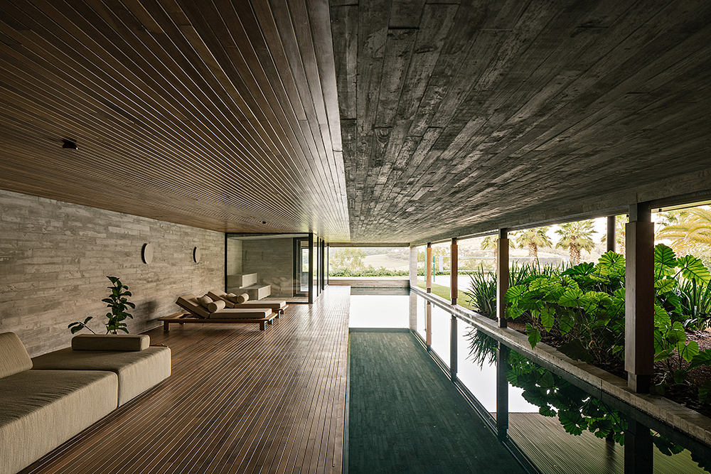 Expansive interior with wooden floors, concrete walls, and a reflection pool overlooking greenery.