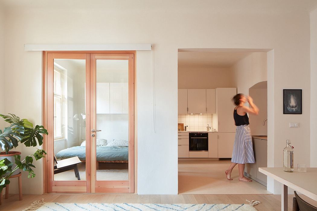 Interior with wooden sliding doors, kitchen, and standing person in striped skirt.