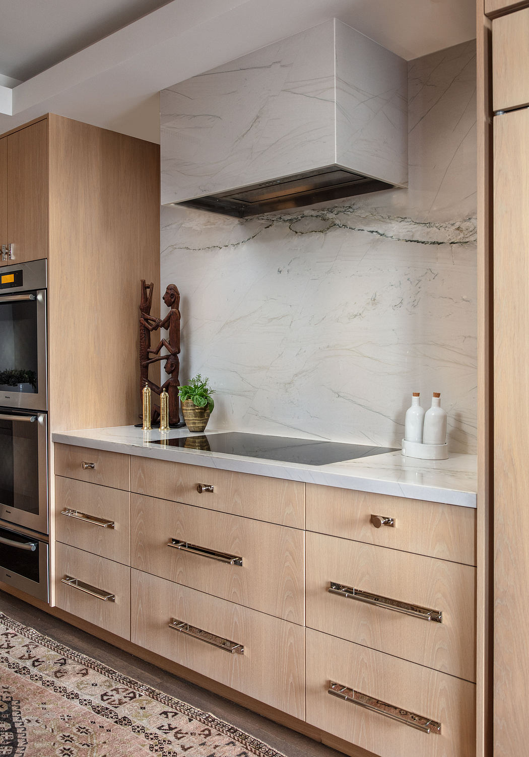Sleek modern kitchen with natural wood cabinetry, marble backsplash, and minimalist decor.