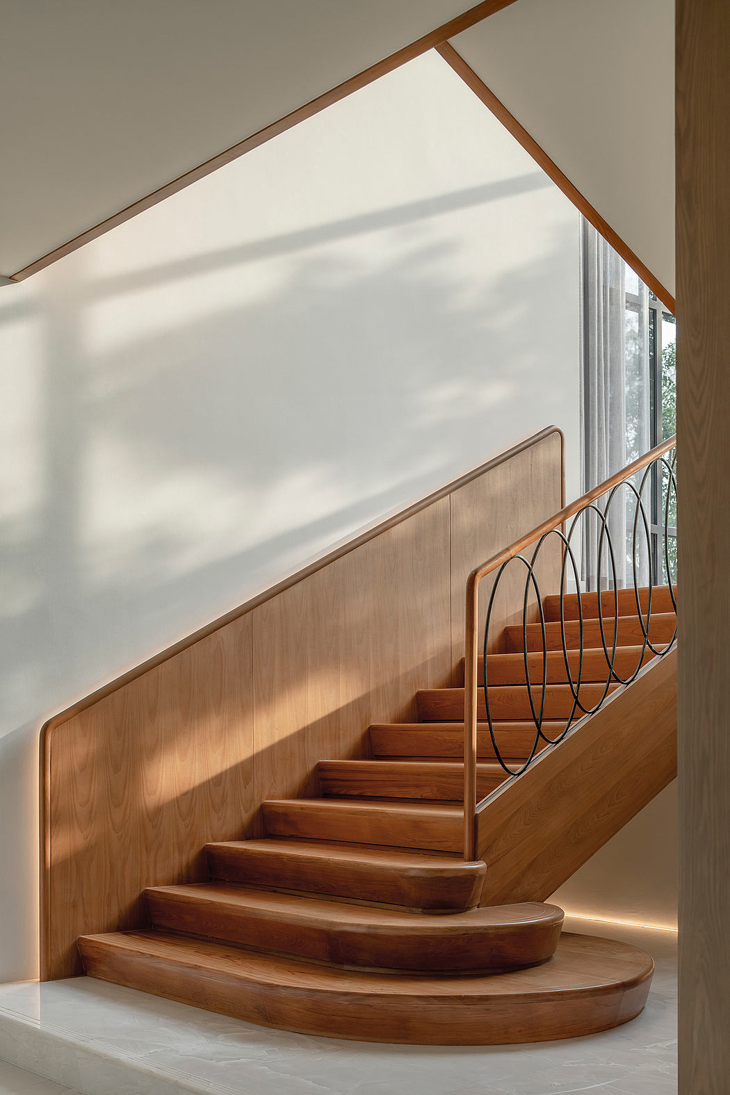 A modern staircase with curved wooden steps and a geometric iron railing.