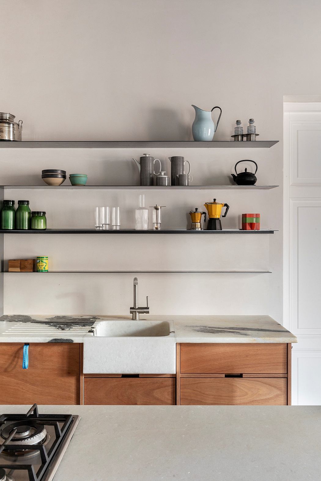 Minimalist kitchen with wooden drawers, floating shelves, and a farmhouse-style sink.