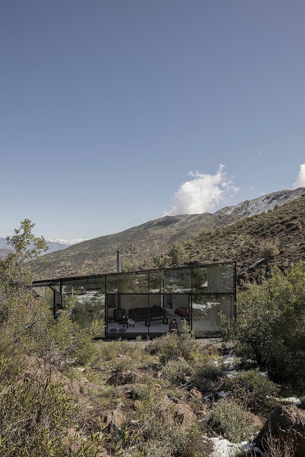 A glass-enclosed cabin nestled in a rugged, mountainous landscape with a serene, natural setting.