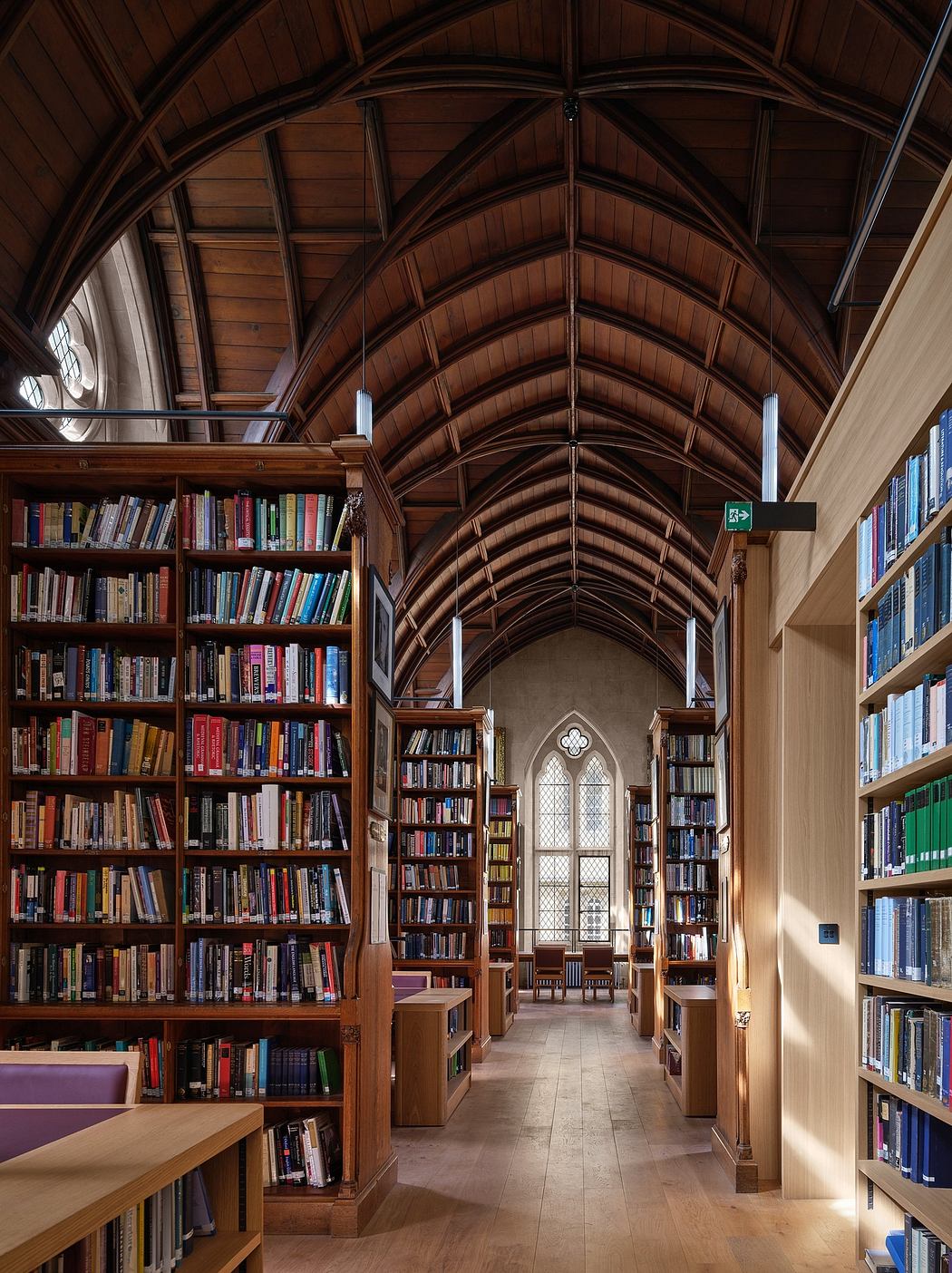 A stunning library with a vaulted wooden ceiling, Gothic-style windows, and towering bookshelves.
