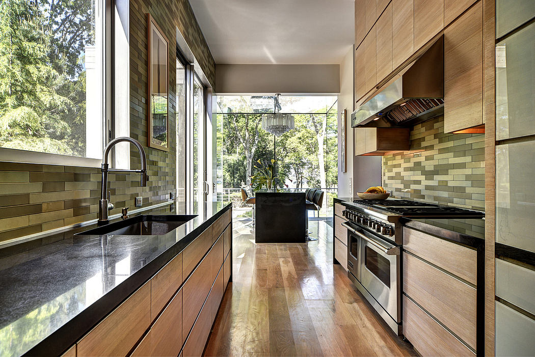 A modern, open-concept kitchen with wood cabinetry, granite countertops, and a view of the lush, wooded surroundings.