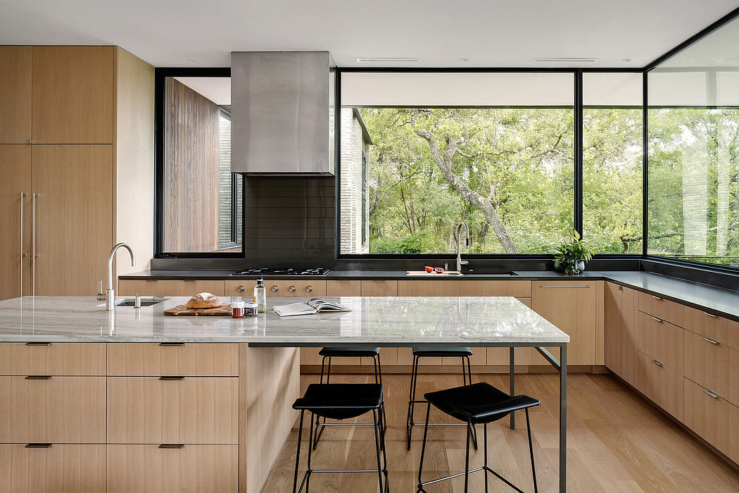 Sleek, modern kitchen with large windows, wooden cabinetry, and black countertops.