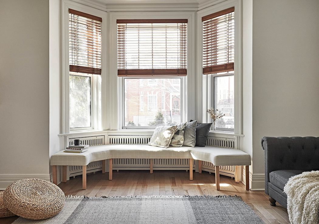 Cozy bay window nook with built-in wood seating, plush cushions, and wood blinds.