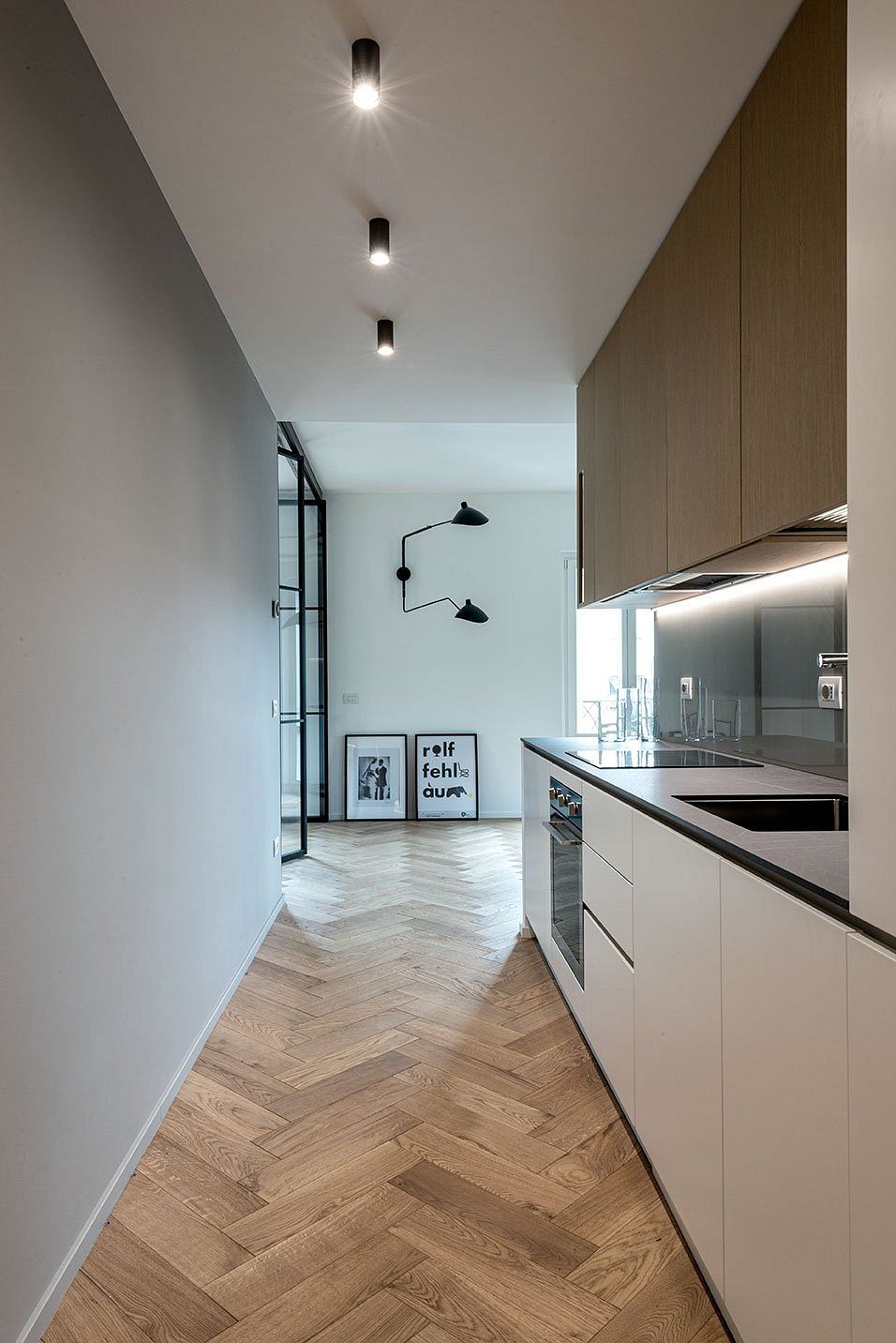 Sleek modern kitchen with herringbone wood floors and minimalist lighting.