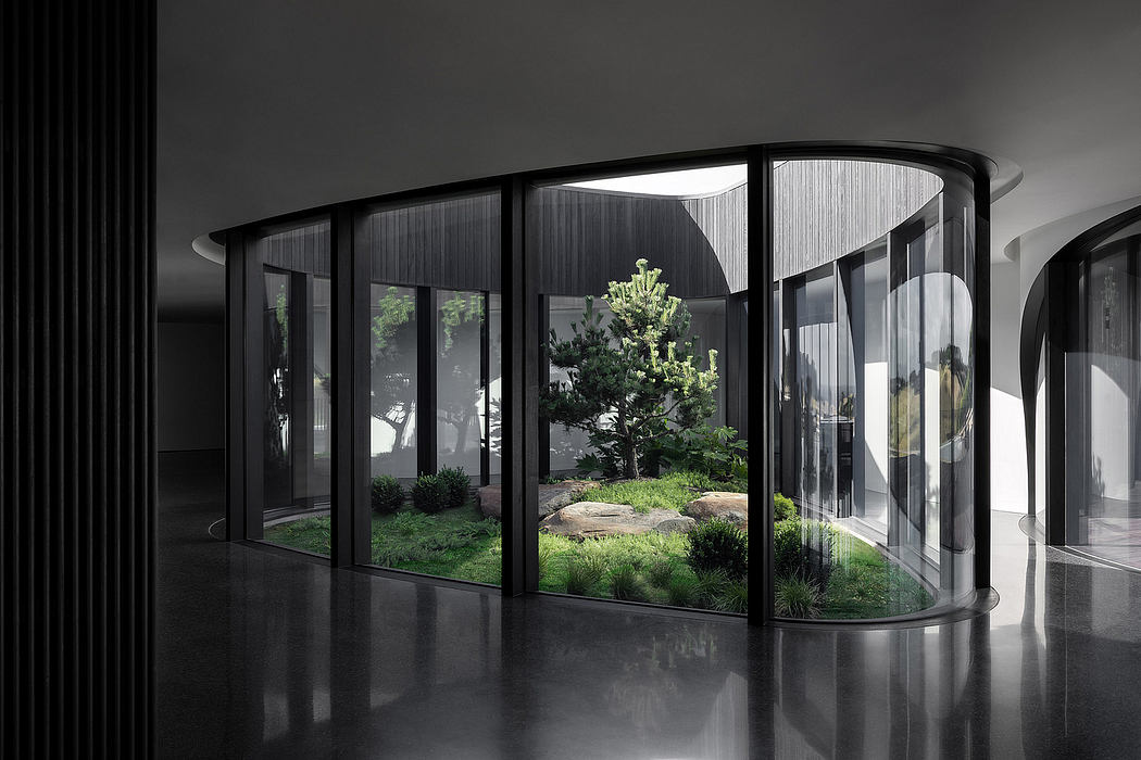 Large curved glass wall enclosing a lush green garden, creating a tranquil indoor-outdoor space.