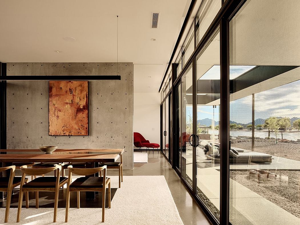 Minimalist dining area with concrete walls, wooden furniture, and large windows showcasing scenic views.