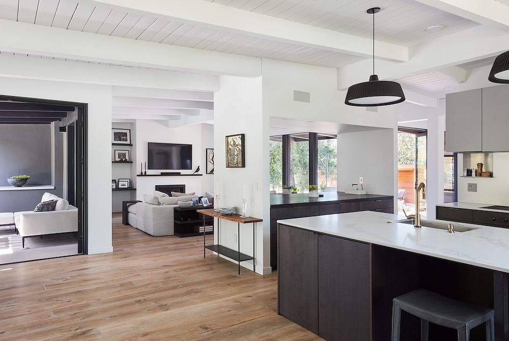 An open floor plan with a modern kitchen, living room, and wood floors. Sleek black and white decor.