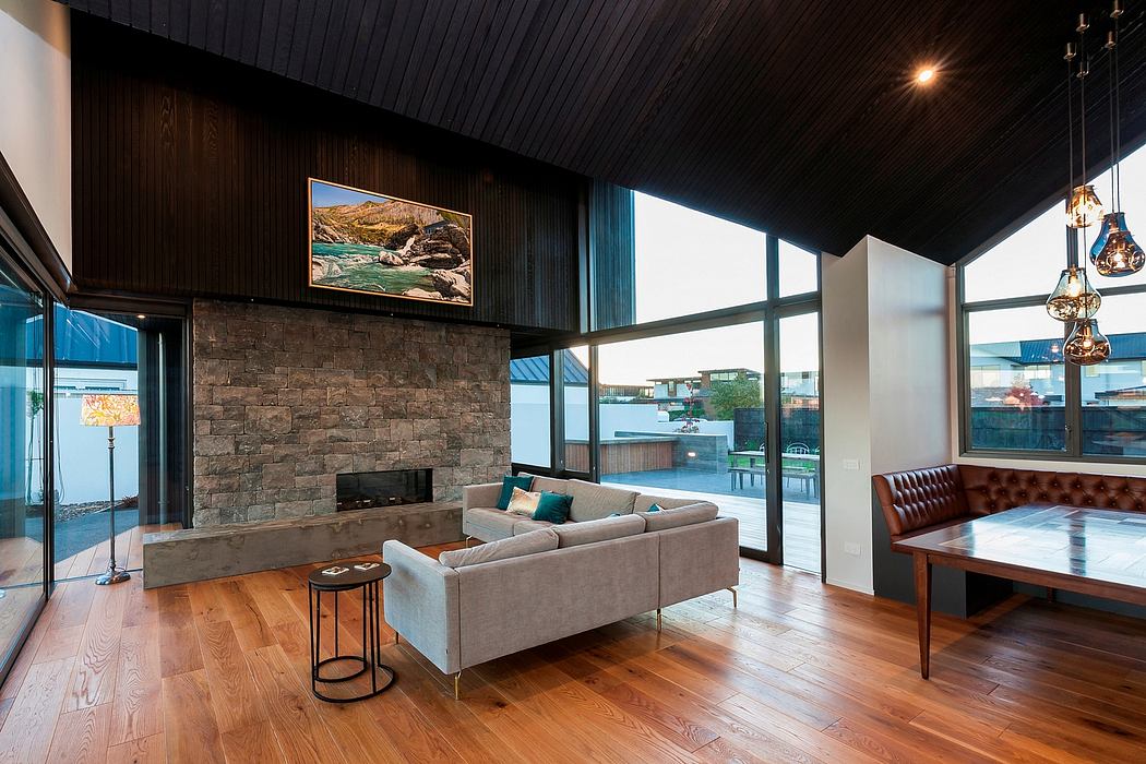 Cozy, modern living room with large windows, stone fireplace, and wooden floors.