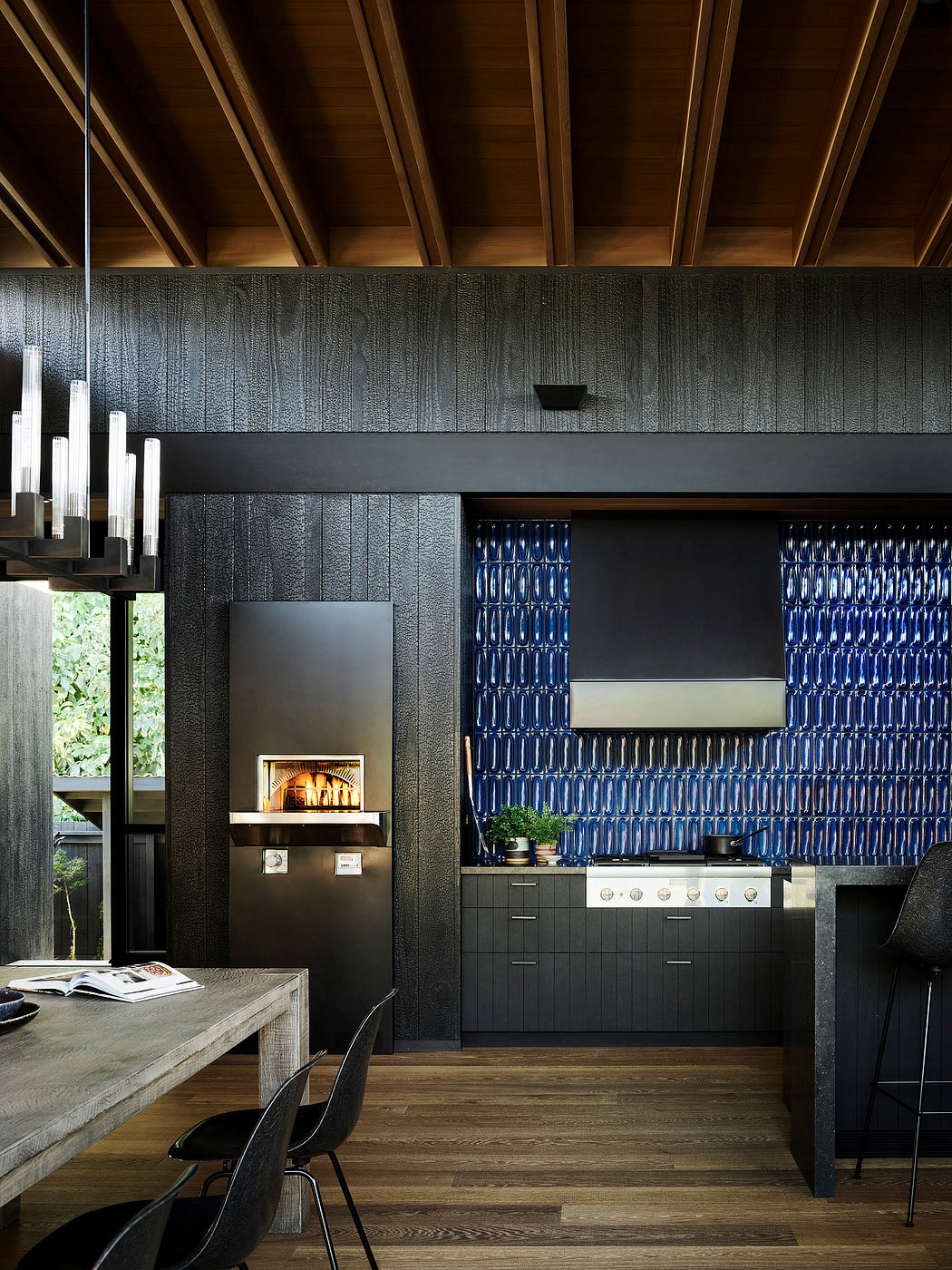 Modern kitchen with sleek black cabinetry, patterned tile backsplash, and a cozy fireplace.