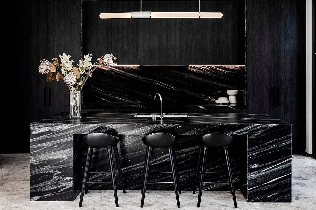 Sleek, modern kitchen with dramatic black marble countertops, minimalist bar stools, and elegant floral arrangement.
