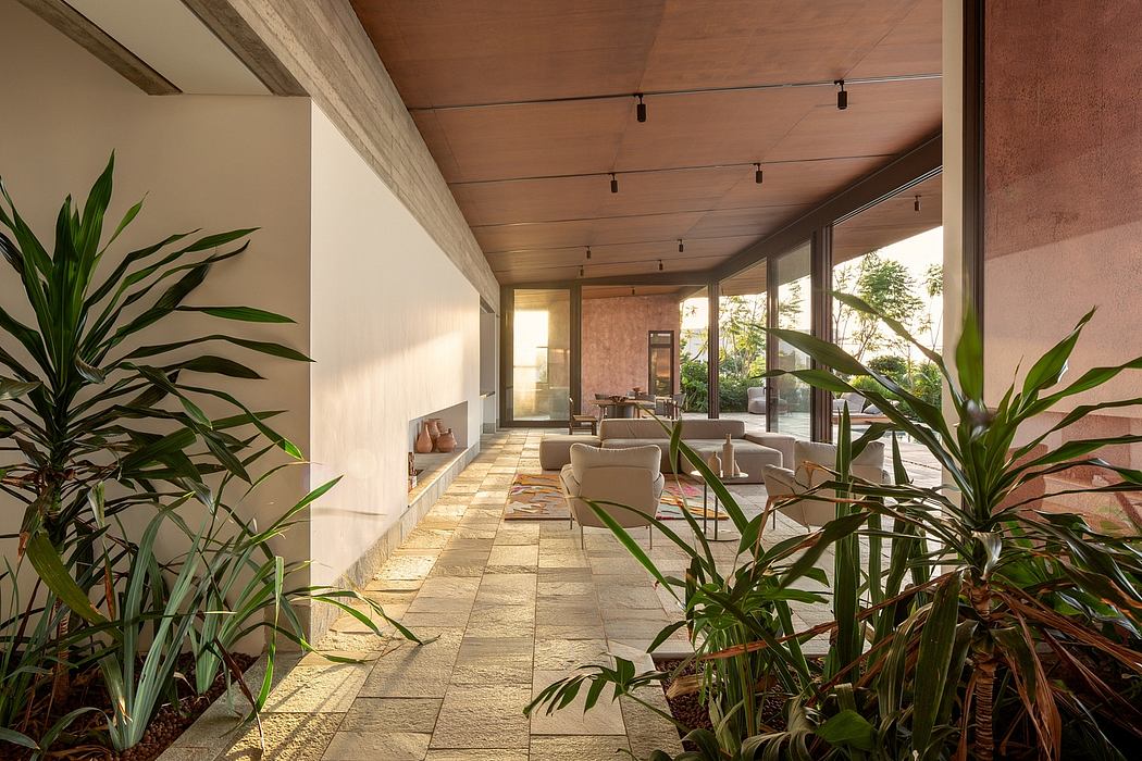 Spacious indoor-outdoor living area with lush tropical plants, floor-to-ceiling windows, and warm wooden accents.